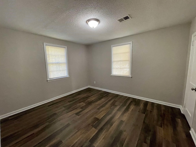 empty room with a healthy amount of sunlight, a textured ceiling, and dark hardwood / wood-style flooring