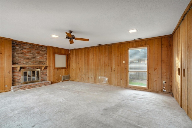 unfurnished living room with light colored carpet, a textured ceiling, a fireplace, and wood walls