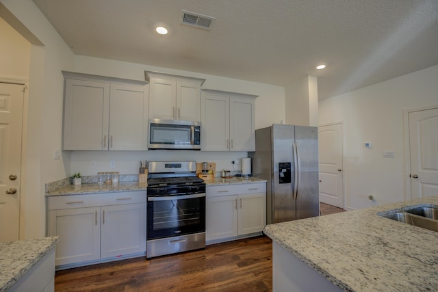 kitchen featuring appliances with stainless steel finishes, sink, a textured ceiling, light stone counters, and dark hardwood / wood-style floors