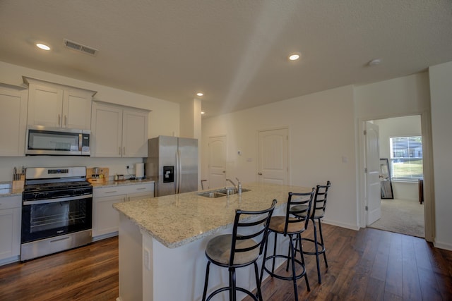 kitchen featuring a center island with sink, sink, light stone countertops, appliances with stainless steel finishes, and dark hardwood / wood-style flooring