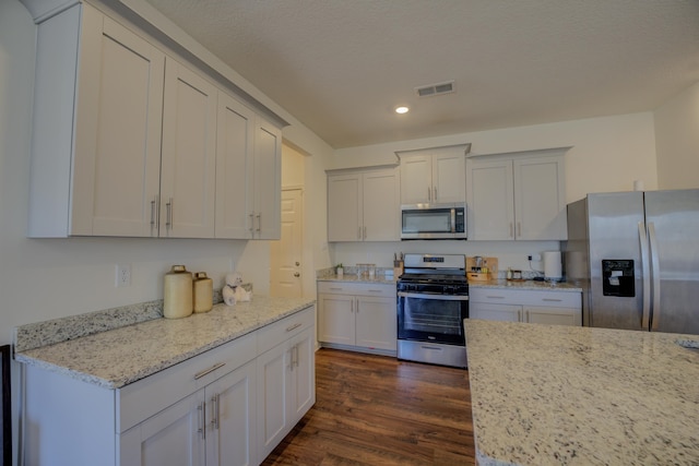 kitchen with dark wood-type flooring, light stone counters, appliances with stainless steel finishes, and white cabinets