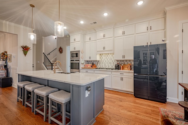 kitchen with an island with sink, sink, white cabinets, light wood-type flooring, and appliances with stainless steel finishes