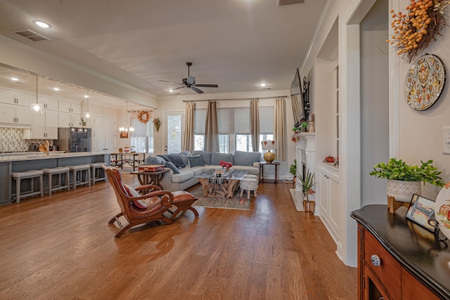 living room with light hardwood / wood-style floors, crown molding, and ceiling fan with notable chandelier