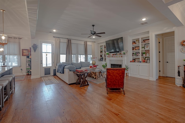 living room with light hardwood / wood-style floors, crown molding, ceiling fan with notable chandelier, and built in shelves