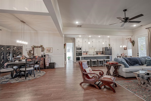 living room with ornamental molding, wood-type flooring, and ceiling fan with notable chandelier