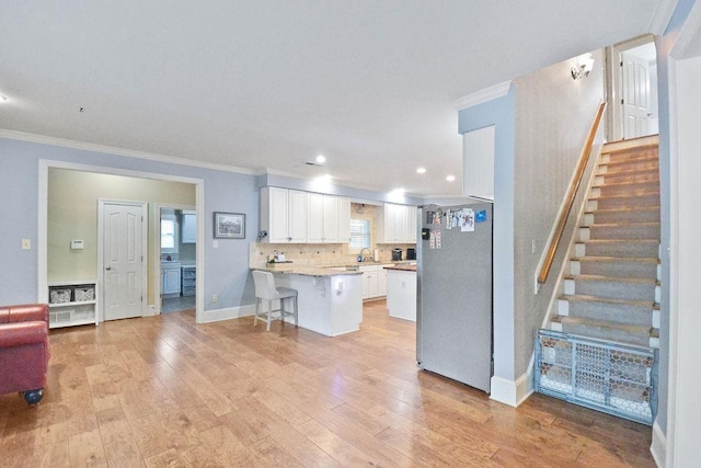kitchen featuring ornamental molding, light wood finished floors, a peninsula, and freestanding refrigerator