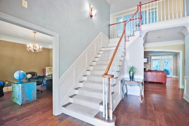staircase featuring ornamental molding, a high ceiling, an inviting chandelier, and wood finished floors