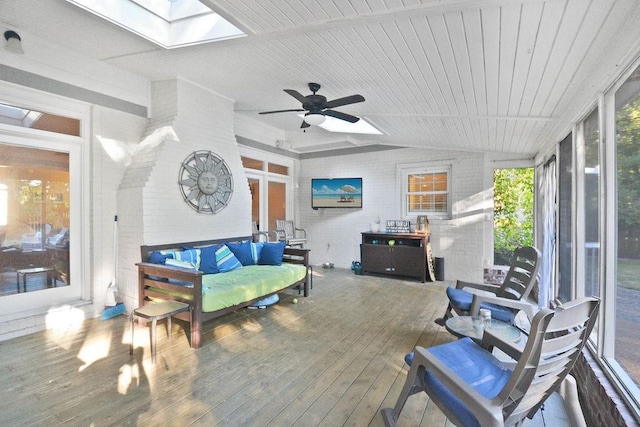sunroom with a deck, hardwood / wood-style flooring, vaulted ceiling with skylight, and brick wall