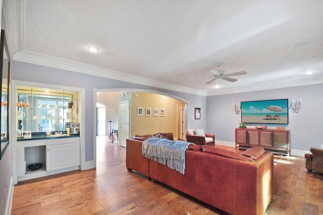 living area featuring light wood finished floors, ceiling fan, crown molding, baseboards, and arched walkways