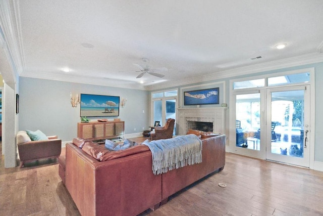 living area with a fireplace, wood finished floors, ceiling fan, and crown molding
