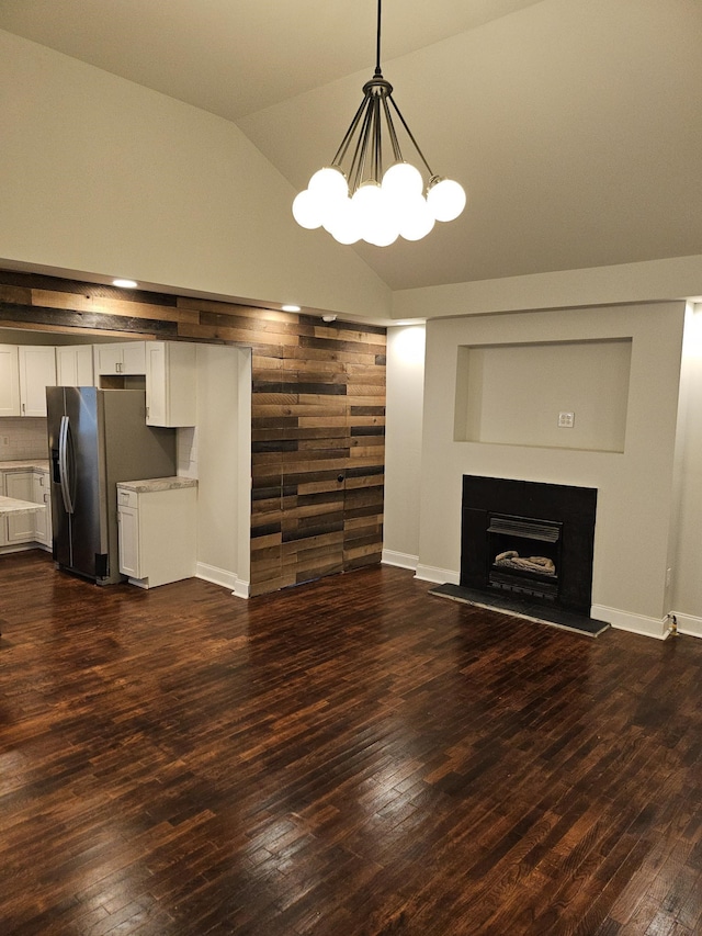 unfurnished living room featuring a notable chandelier, dark wood-type flooring, and vaulted ceiling