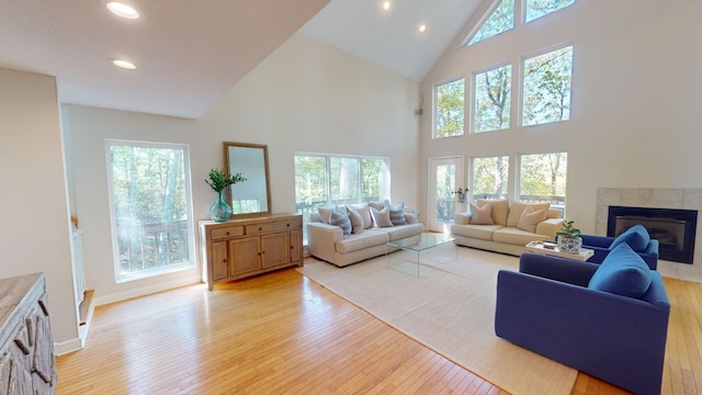 living room featuring a tiled fireplace, high vaulted ceiling, and light hardwood / wood-style flooring