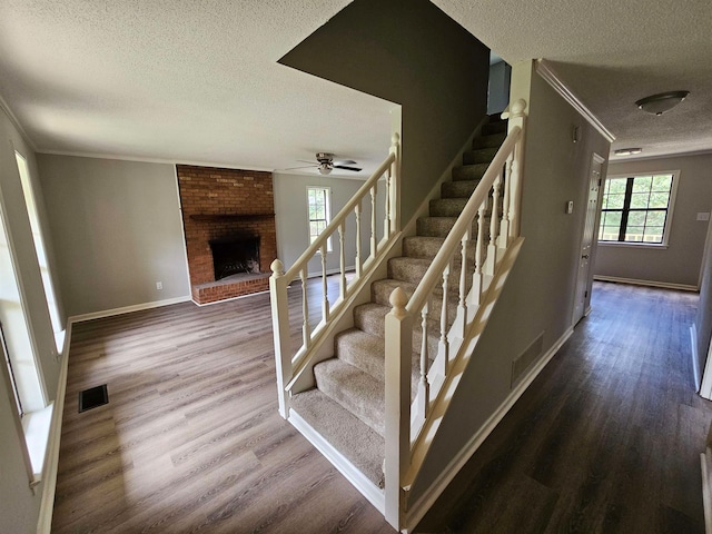 staircase with a textured ceiling, a fireplace, wood finished floors, visible vents, and ornamental molding