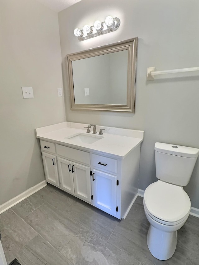 half bath featuring baseboards, vanity, and toilet