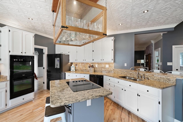 kitchen with a kitchen island, light stone countertops, light hardwood / wood-style floors, crown molding, and sink