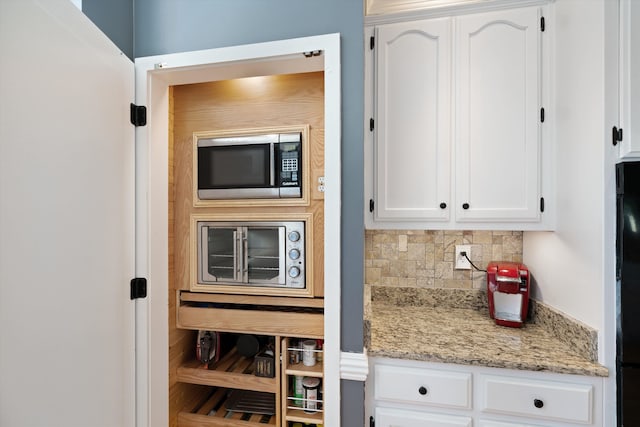 kitchen featuring decorative backsplash, white cabinets, light stone counters, and stainless steel microwave