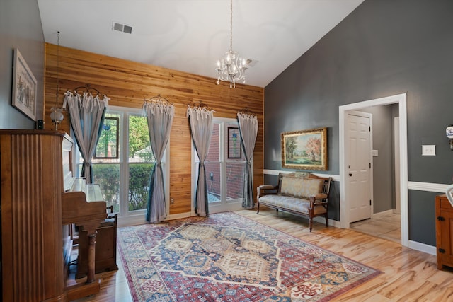 sitting room with light hardwood / wood-style floors, a notable chandelier, wood walls, and high vaulted ceiling