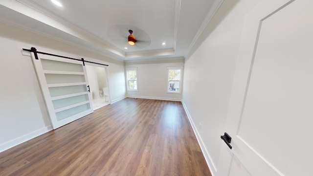 unfurnished bedroom featuring a tray ceiling, a barn door, hardwood / wood-style flooring, and crown molding