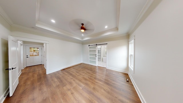 unfurnished room featuring a barn door, baseboards, a raised ceiling, ceiling fan, and wood finished floors