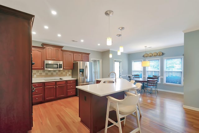 kitchen with appliances with stainless steel finishes, a kitchen bar, an island with sink, pendant lighting, and light hardwood / wood-style flooring