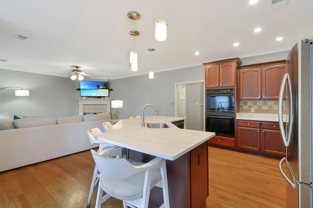 kitchen featuring backsplash, sink, decorative light fixtures, light wood-type flooring, and stainless steel refrigerator