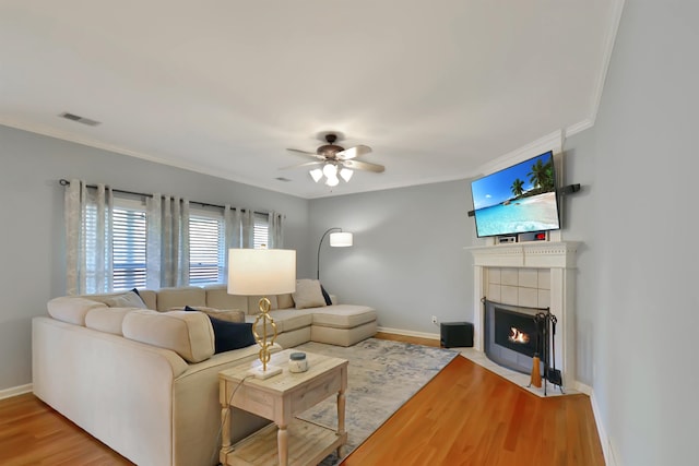 living room featuring crown molding, hardwood / wood-style flooring, a tile fireplace, and ceiling fan