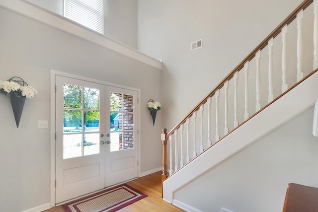 foyer with a high ceiling, light wood-type flooring, and french doors