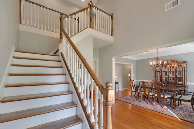 stairway featuring wood-type flooring, a high ceiling, and a chandelier