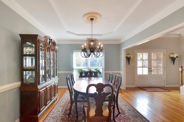 dining area featuring french doors, a raised ceiling, light hardwood / wood-style floors, a notable chandelier, and ornamental molding