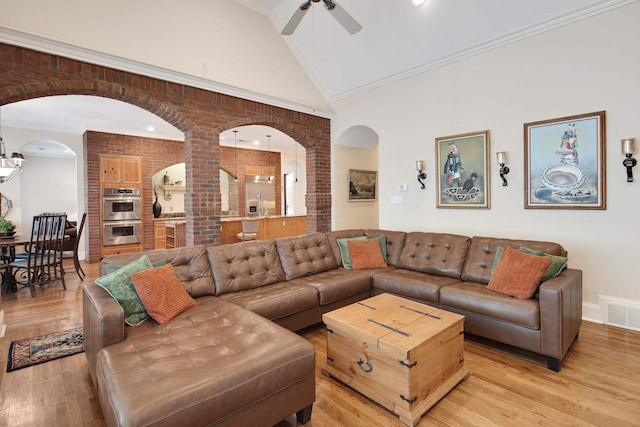 living room featuring ceiling fan, high vaulted ceiling, light hardwood / wood-style flooring, ornamental molding, and brick wall