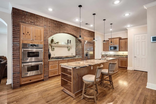 kitchen with a large island, built in appliances, hardwood / wood-style flooring, a breakfast bar, and brick wall