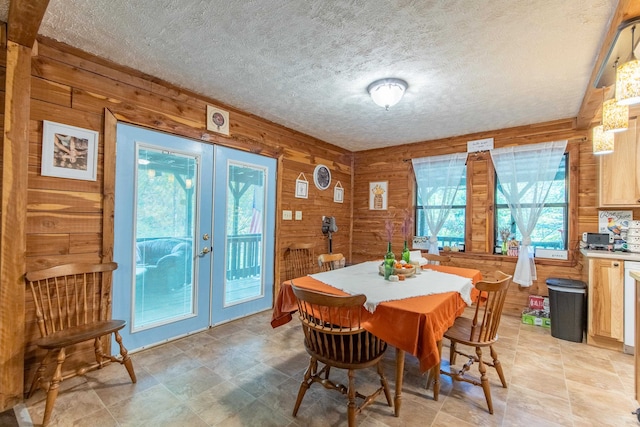 dining room featuring wooden walls, a textured ceiling, and french doors