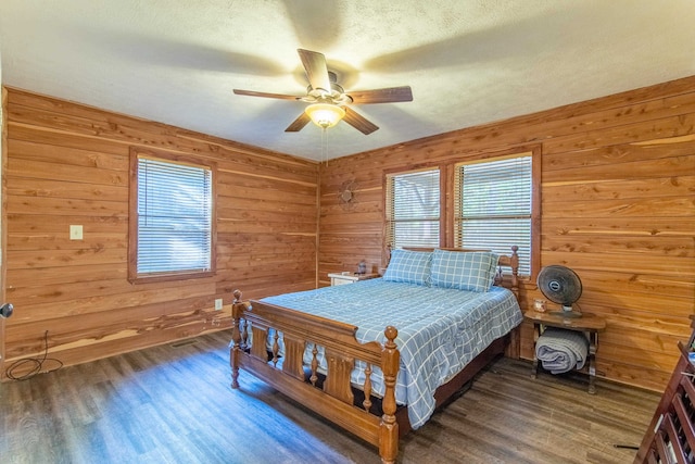 bedroom with ceiling fan, dark hardwood / wood-style flooring, and wooden walls