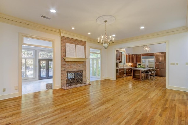 unfurnished living room with ornamental molding, sink, a brick fireplace, a chandelier, and light hardwood / wood-style floors