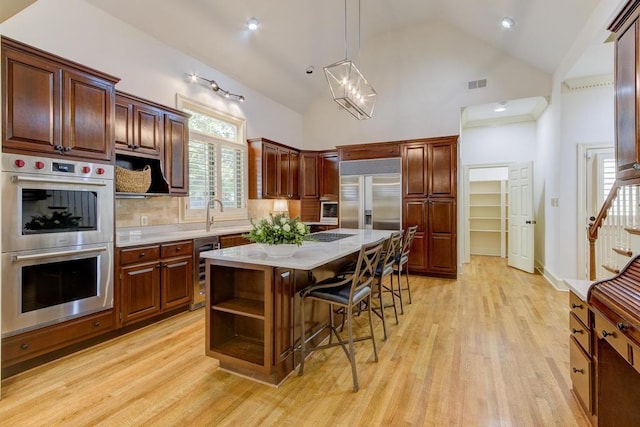 kitchen with a kitchen island, a breakfast bar, light wood-type flooring, appliances with stainless steel finishes, and high vaulted ceiling