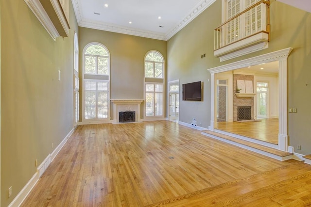 unfurnished living room featuring light hardwood / wood-style floors, crown molding, and a towering ceiling