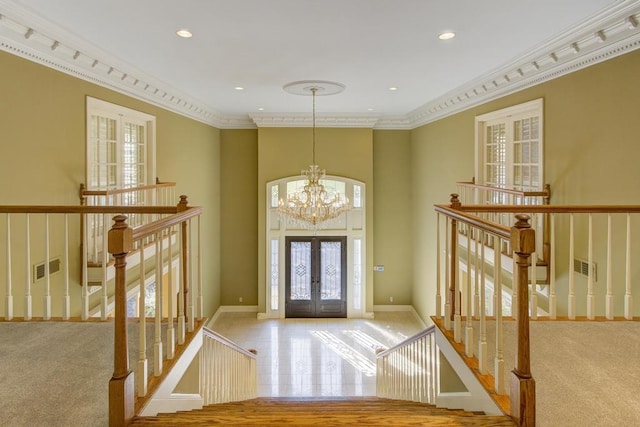 carpeted entrance foyer featuring french doors, ornamental molding, and a notable chandelier