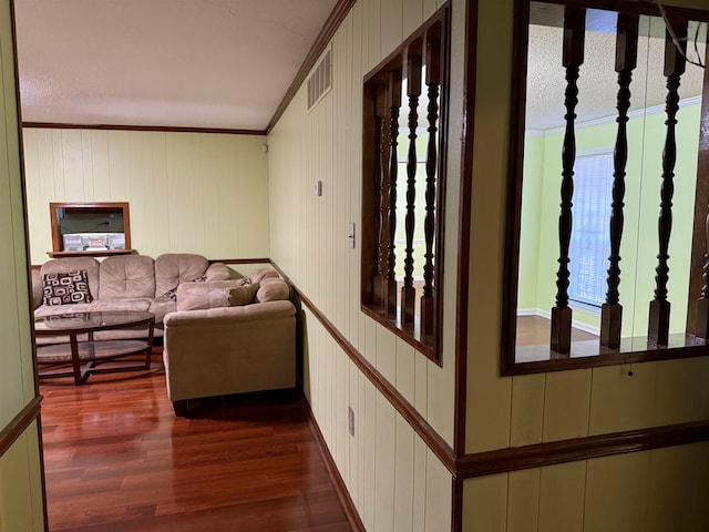 hallway featuring dark wood-type flooring, wood walls, ornamental molding, and a wealth of natural light