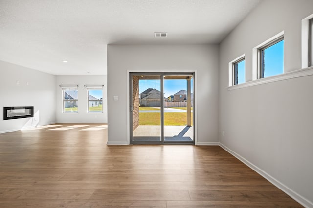 unfurnished living room with a healthy amount of sunlight, wood-type flooring, and a textured ceiling