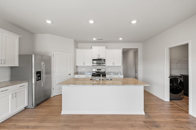 kitchen with a center island with sink, white cabinets, stainless steel appliances, and light wood-type flooring