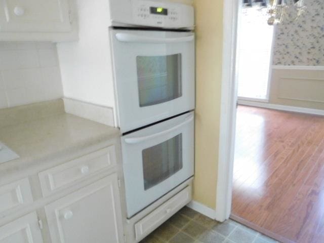 kitchen featuring an inviting chandelier, white cabinetry, double oven, and hardwood / wood-style flooring