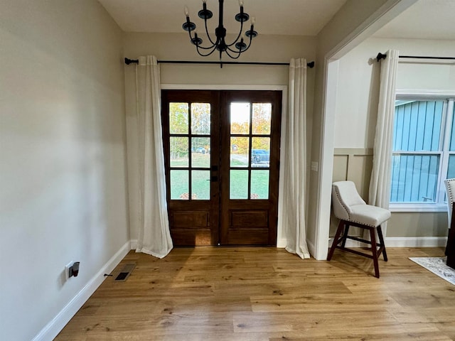 doorway to outside featuring a wealth of natural light, french doors, an inviting chandelier, and light wood-type flooring