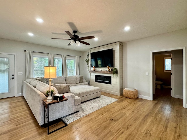 living room featuring a textured ceiling, ceiling fan, light hardwood / wood-style flooring, and a fireplace