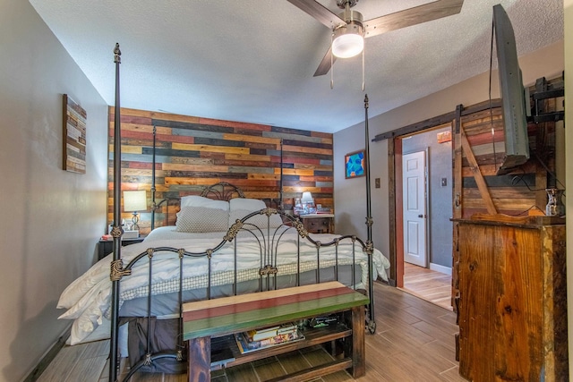 bedroom with wood walls, a barn door, a textured ceiling, ceiling fan, and hardwood / wood-style flooring