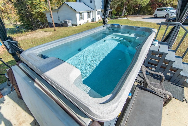 view of pool with a hot tub, a lawn, and central AC unit