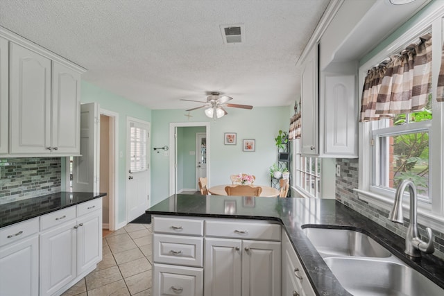 kitchen with tasteful backsplash, sink, kitchen peninsula, white cabinets, and light tile patterned floors