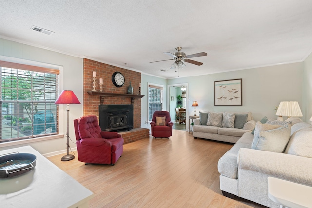 living room featuring ornamental molding, a textured ceiling, light wood-type flooring, and a fireplace