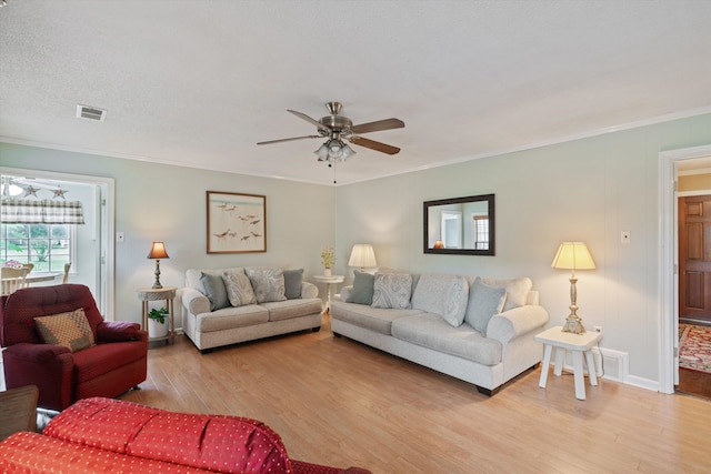 living room featuring ceiling fan, a textured ceiling, ornamental molding, and light hardwood / wood-style flooring