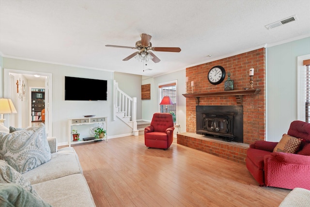 living room with ceiling fan, a textured ceiling, light wood-type flooring, crown molding, and a wood stove