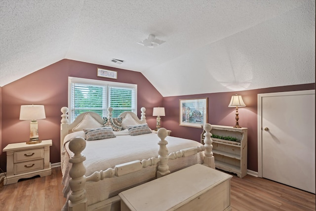 bedroom with light hardwood / wood-style floors, a textured ceiling, and vaulted ceiling